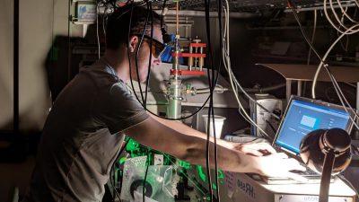 亚尼克Pleimling, 佩戴护目镜, 在一个充满设备的黑暗实验室里对着电脑工作.